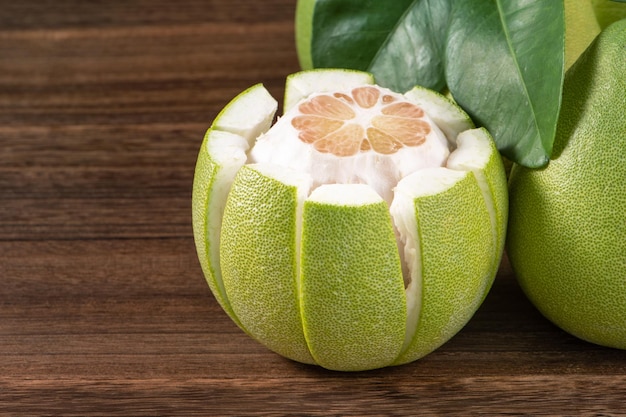 Fresh peeled pomelo grapefruit shaddock with green leaves on dark wooden plank table Seasonal fruit near midautumn festival close up copy space