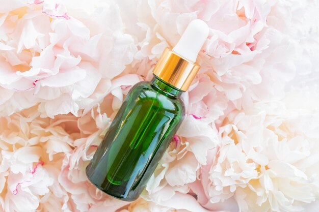 Fresh peony flowers background and bottle with cosmetic oil for branding Wellness home skin care and spa relax treatment concept Mockup package