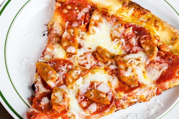 Fresh pepperoni and sausage pizza slice on the table in Italian restaurant.