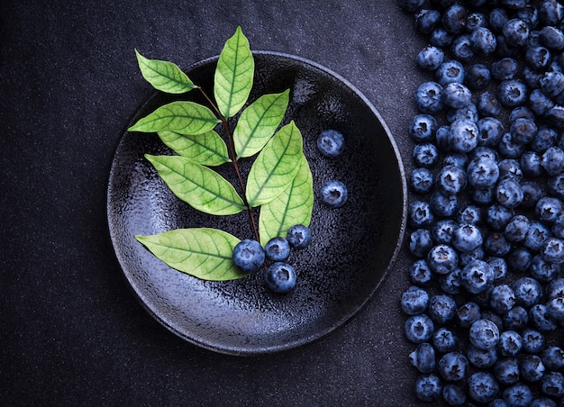  fresh picked blueberries with green of leaf on black stone background