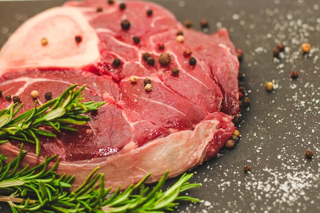 Fresh piece of meat beef steak on the bone ossobuco with a sprig of rosemary on a black background