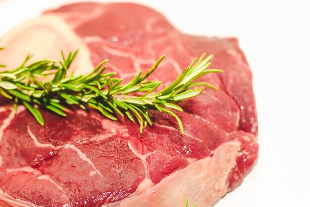 Свежий кусок мяса большой говяжий стейк на кости оссобуко с веточкой розмарина