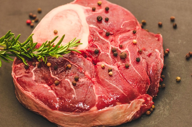 Fresh piece of meat large beef steak on the bone ossobuco with a sprig of rosemary on a black background