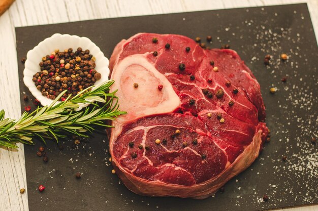 黒の背景にローズマリーの小枝と骨 ossobuco に大きな牛肉ステーキの新鮮な部分
