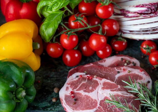 Fresh piece of meat, spices and assorted vegetables on dark green marble board