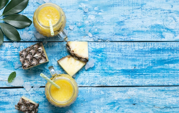 Fresh pineapple smoothie in glasses with straws on a blue wooden rustic background