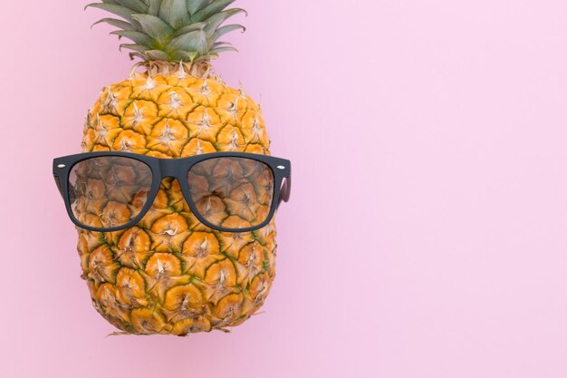 Fresh pineapple wearing sunglasses on a bright pink background