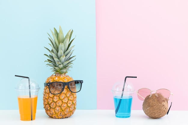 Свежий ананас с солнцезащитными очками рядом со стаканом сока и коктейльной соломинкой на цветном фоне
