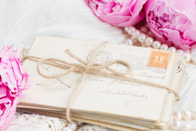 Fresh pink peonies with pile of old mail and pearls