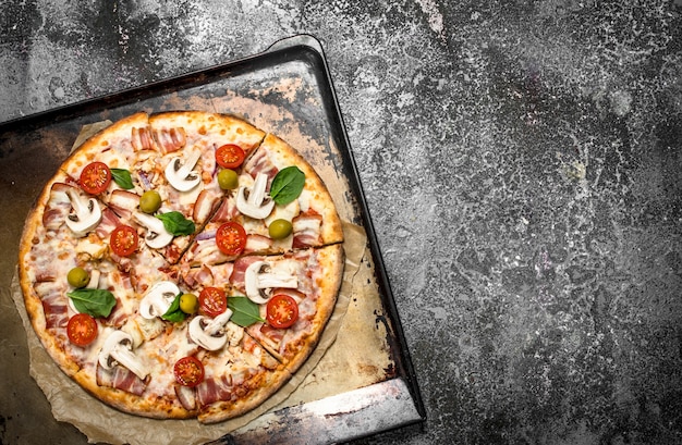 Fresh pizza on a baking sheet. On a rustic background.