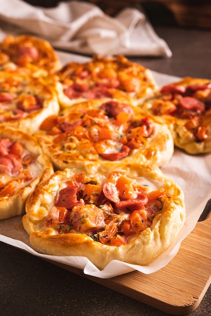 Свежие пиццевые пироги с помидорами, сыром и колбасами на деревянной доске в вертикальном виде