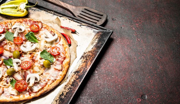 Fresh pizza with mushrooms, bacon and tomatoes. On a rustic background.