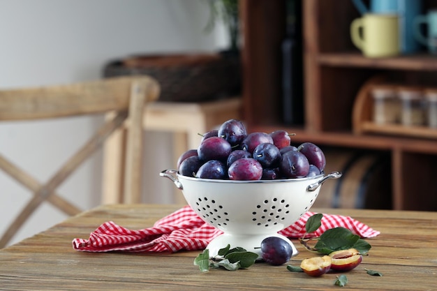 Fresh plums in colander on table