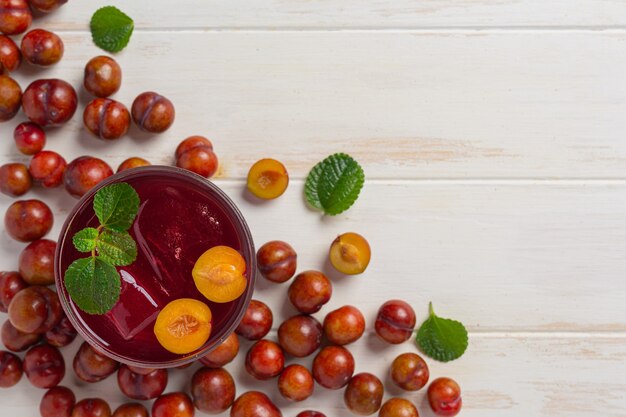 Fresh plums juice on the white wooden surface.