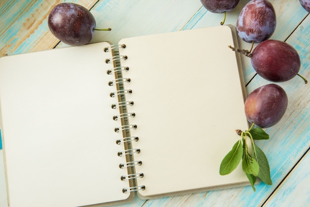 Fresh plums and white notebook on wooden table. Copy space