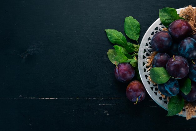 Fresh plums with leaves Fruits On a black wooden background Top view Free space for your text