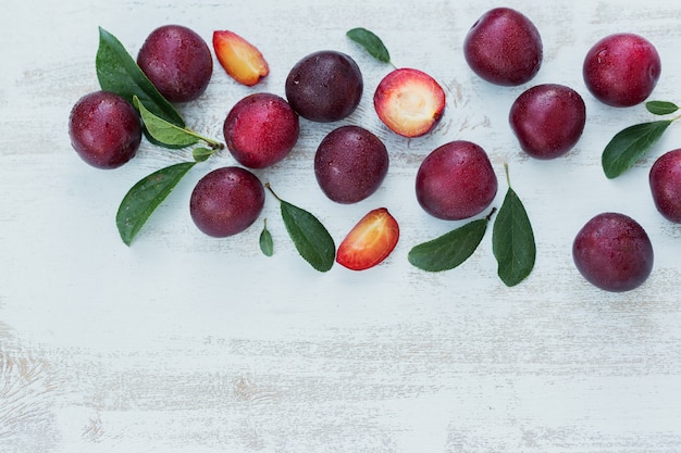 Fresh plums with leaves on white rustic wooden table background. Autumn harvest concept. Flat lay with copy space for text