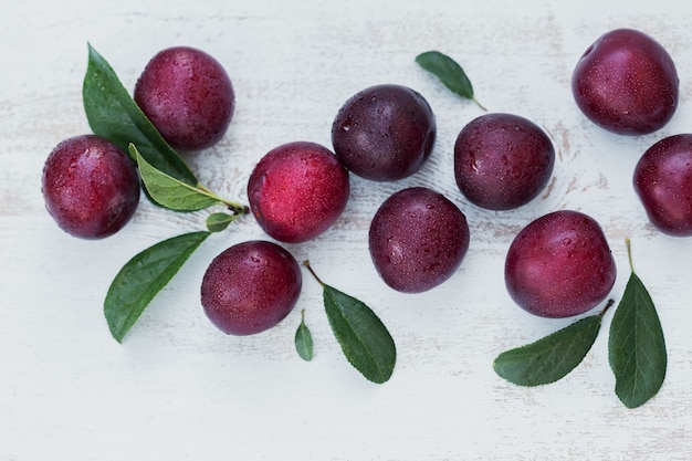 Fresh plums with leaves on white rustic wooden table background. Autumn harvest concept. Top view