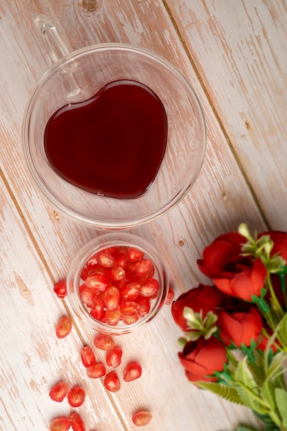 Свежий гранатовый сок подается в стакане в форме сердца со свежими фруктами граната на деревянном столе