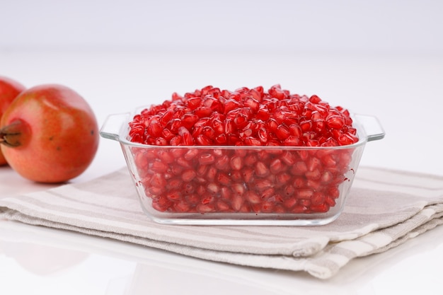 Fresh Pomegranate seed arranged in a square glass container with fresh fruit placed beside it