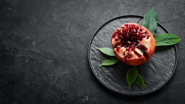 Fresh pomegranate with leaves on black stone background Fruits Top view Free space for your text