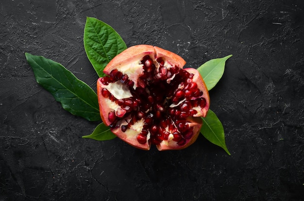 Fresh pomegranate with leaves on black stone background Fruits Top view Free space for your text