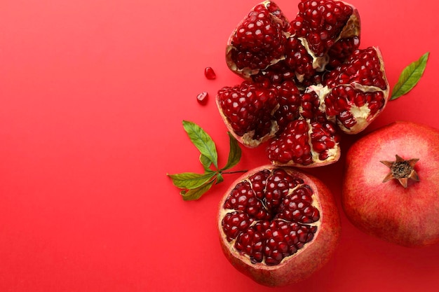 fresh pomegranates and green leaves on red background flat lay space for text