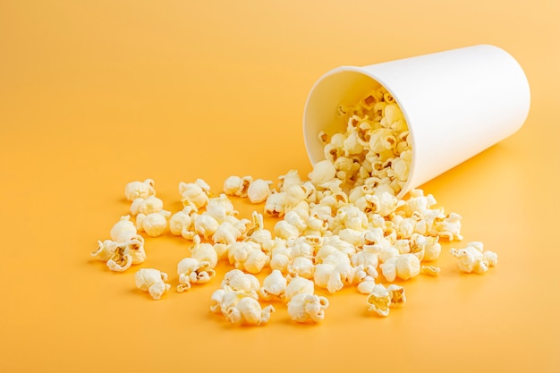 Popcorn fresco versato fuori dalla scatola bianca su uno sfondo arancione. concetto di snack cinematografici. il cibo per guardare un film e intrattenimento, da vicino. mocap scatola popcorn