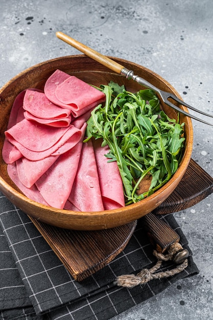 Fresh pork ham slices in wooden plate with arugula salad Gray background Top view