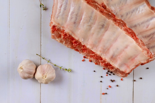 Свежие свиные ребрышки, приготовленный для мяса маринад для жаркого с чесноком, душистым перцем и розмарином на деревянной доске