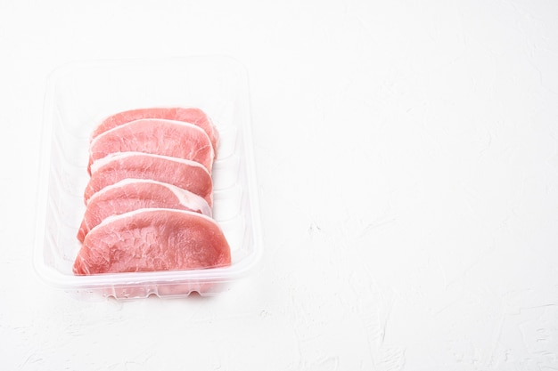 Fresh pork set, in plastic pack container, on white stone table background, with copy space for text