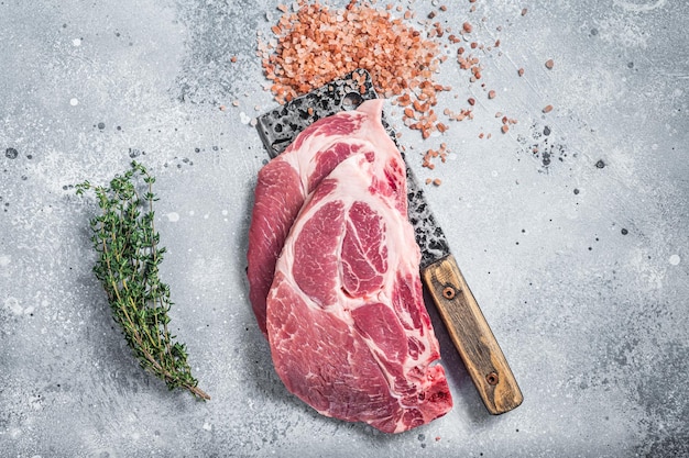 Fresh pork tender steaks from raw neck meat on butcher meat cleaver with salt and thyme Gray background Top view