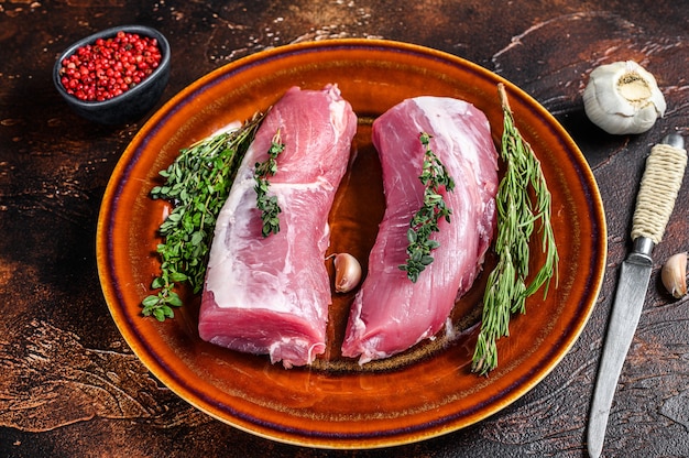 Fresh pork tenderloin meat with rosemary and thyme. Dark background. Top view.