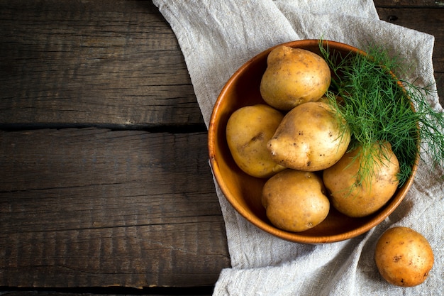 Fresh potatoes in a bowl on the old wooden table. Top view with copy space