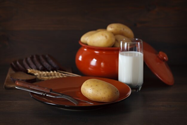 Fresh potatoes in a clay plate on a background of the dark wooden surface.