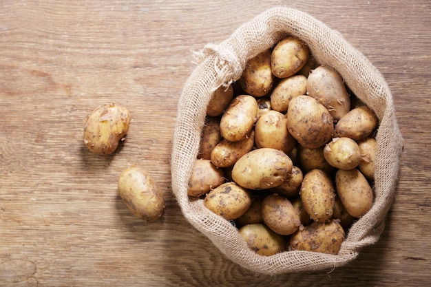 Fresh potatoes in a sack on wooden table