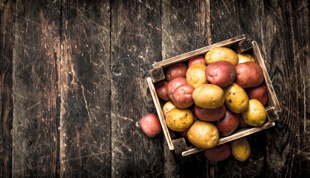 Fresh potatoes in a wooden box. On a wooden background.