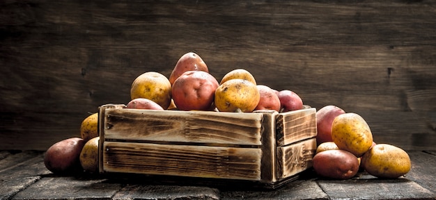 Fresh potatoes in a wooden box. On a wooden background.