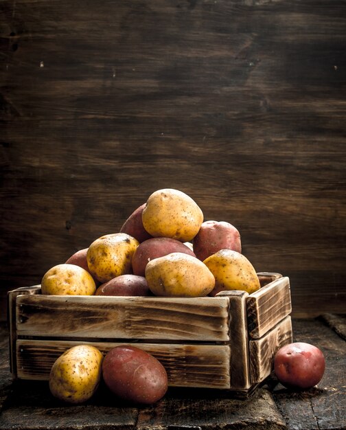 Fresh potatoes in a wooden box on a wooden background