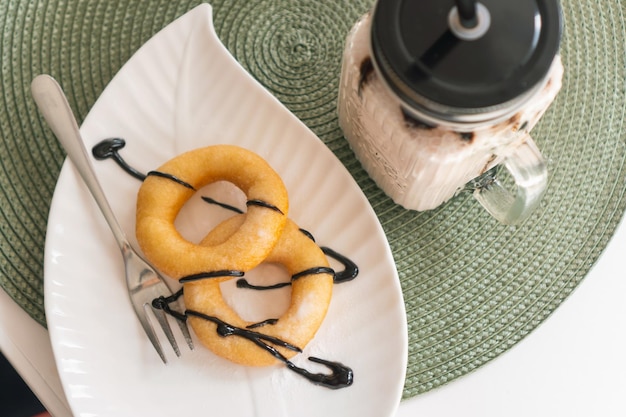 Ciambelle fresche di zucchero a velo con cioccolato e frullato di latte in barattolo di vetro sul tavolo di legno nella caffetteria