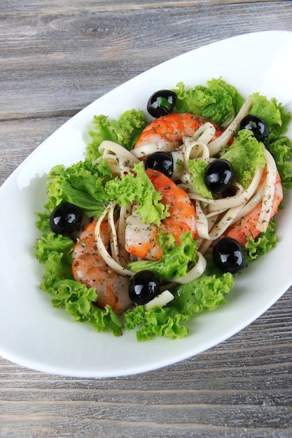 Fresh prawns with spaghetti olives and lettuce in a white oval bowl on wooden background