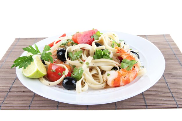 Fresh prawns with spaghetti olives tomatoes and parsley in a big round plate on a napkin on white background isolated