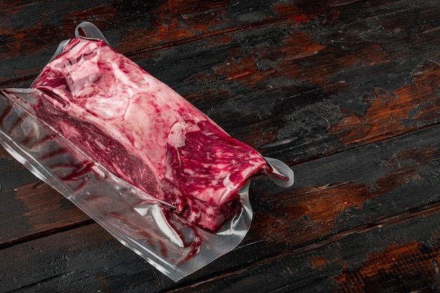 Fresco e premium rib eye tagliato intero in un pacchetto di confezioni sottovuoto, su un vecchio sfondo di tavolo in legno scuro, con copia spazio per il testo