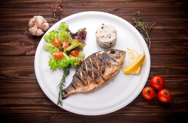 Fresh prepared dorado or sea bream fish with lemon, herbs on wooden background