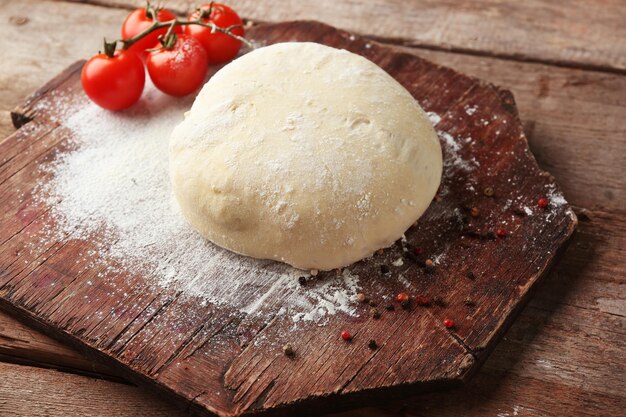 Fresh prepared dough with tomatoes on a wooden board close up