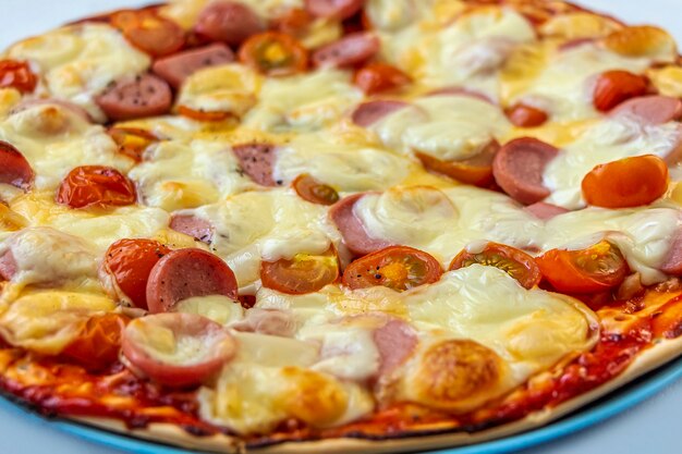 Fresh prepared tasty homemade pizza with tomatoes cherry, sausages and cheese close up.