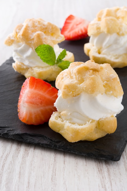 Fresh profiteroles with cream and strawberry on white wooden table