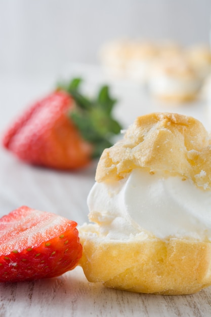 Fresh profiteroles with cream and strawberry on white wooden table