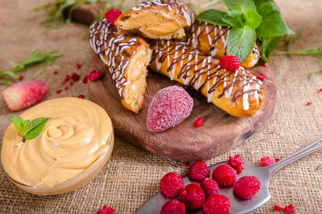 Fresh profitler eclairs lie on a wooden vintage cutting board, in a bowl of condensed milk boiled