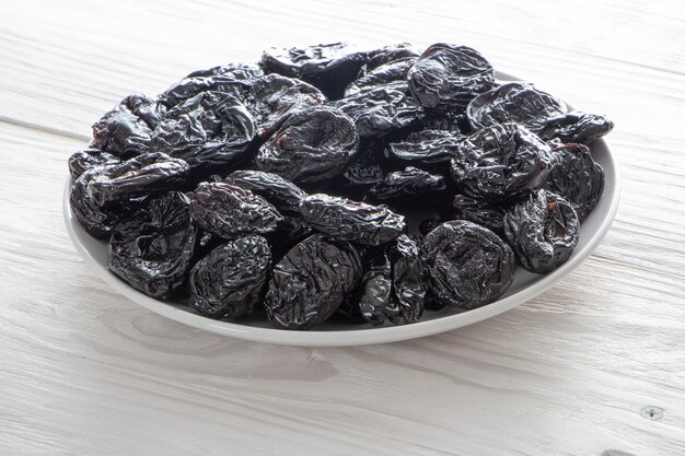 Fresh prunes, an ingredient for healthy eating. Dried plums in white ceramic plate on wooden rustic table.